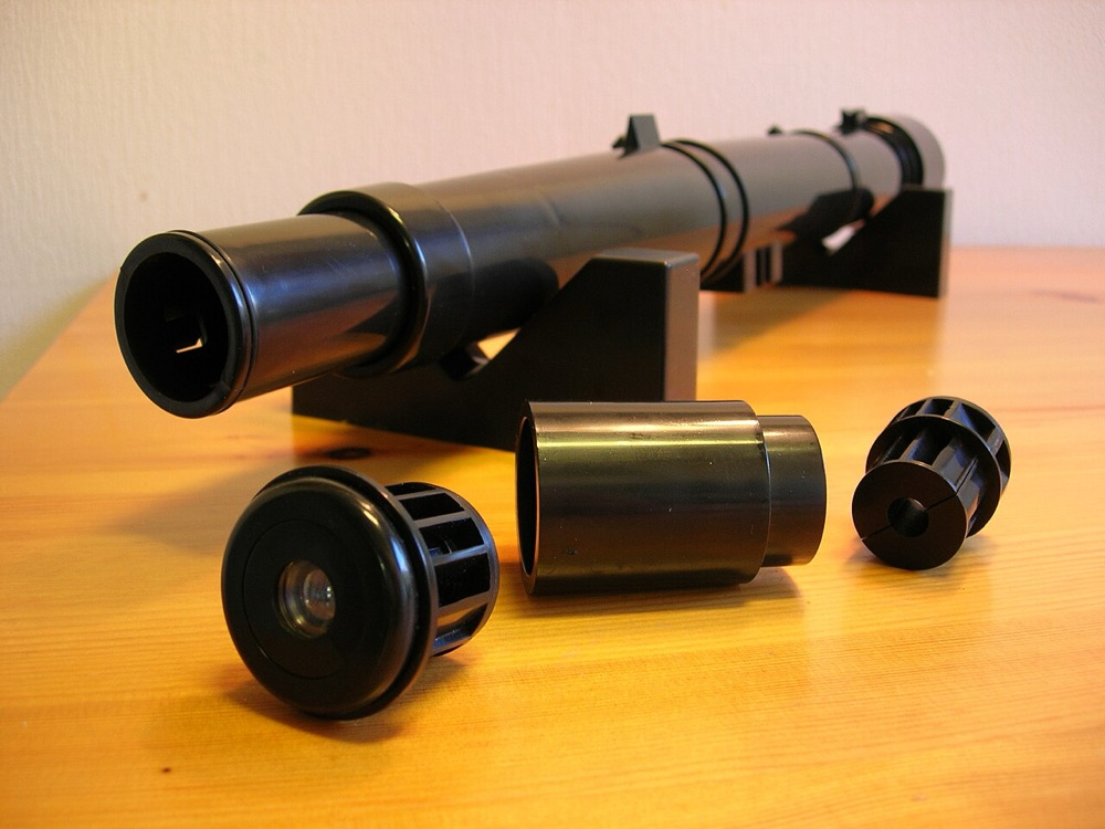 Tube d'une lunette astronomique de démonstration posé sur une table, avec ses oculaires et accessoires démontés devant lui