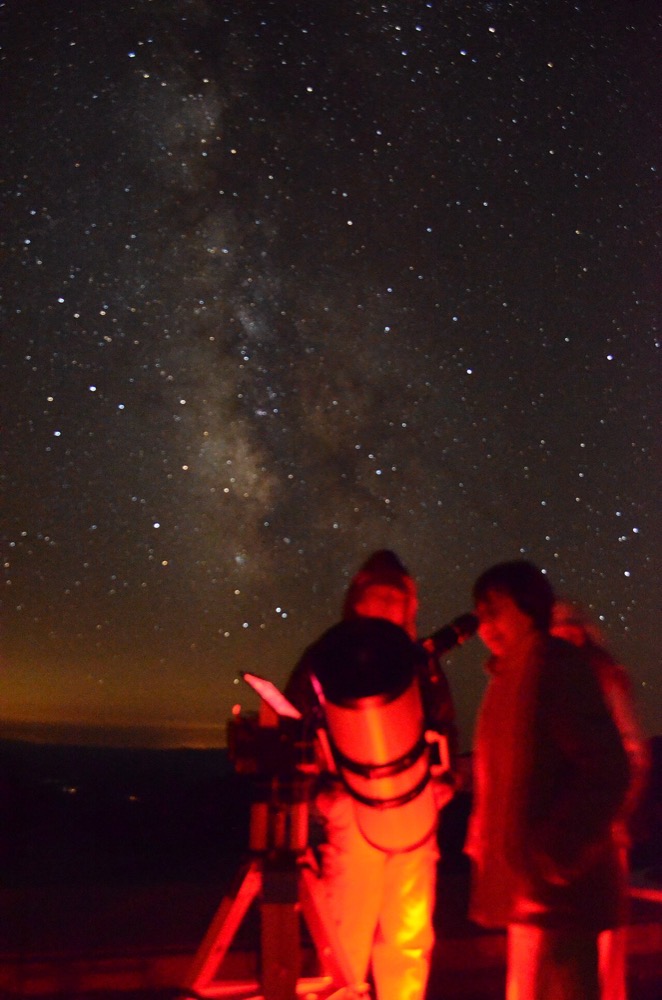 Observateurs autour d'un télescope de Newton sur trépied, sous la Voie lactée